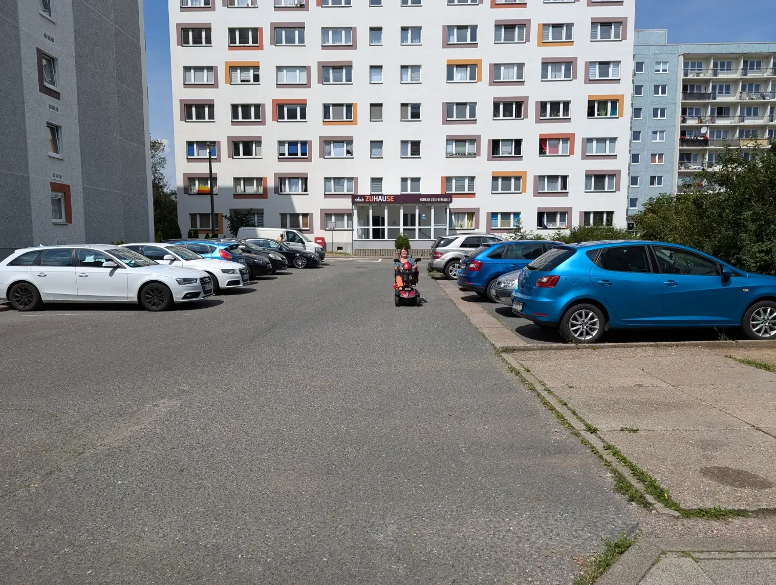 Zu sehen ist die Konrad-Zuse-Straße 5 mit parkenden Autos und einem Senioren-Mobil auf der Straße.