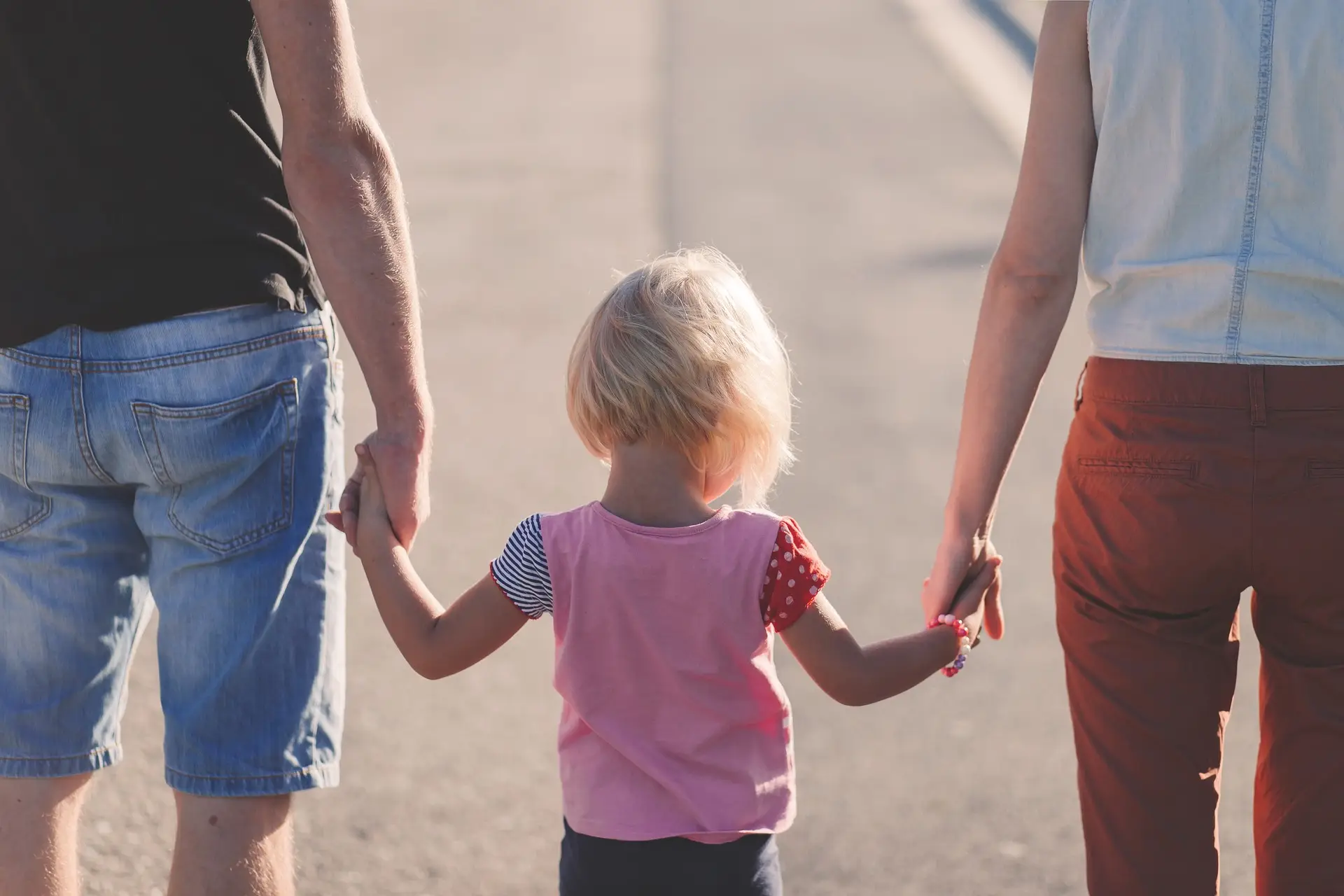 Vater, Mutter und Kind halten die Hand.